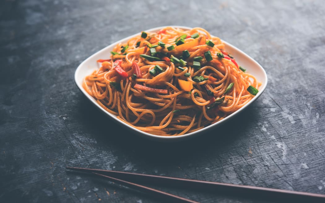 Schezwan Noodles or vegetable Hakka Noodles or chow mein is a popular Indo-Chinese recipes, served in a bowl or plate with wooden chopsticks. selective focus