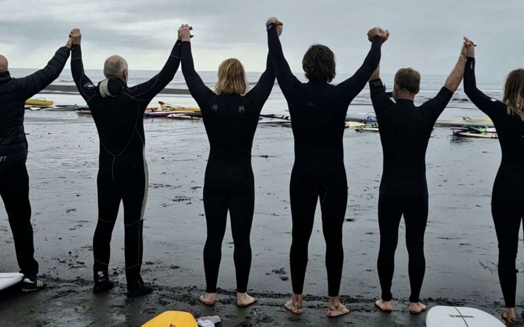 surfers holding hands at East End beach, New Plymouth