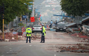 Police stand by amid fallen debris in a cordoned-off street in Christchurch on February 23, 2011 a day after the deadly earthquake.