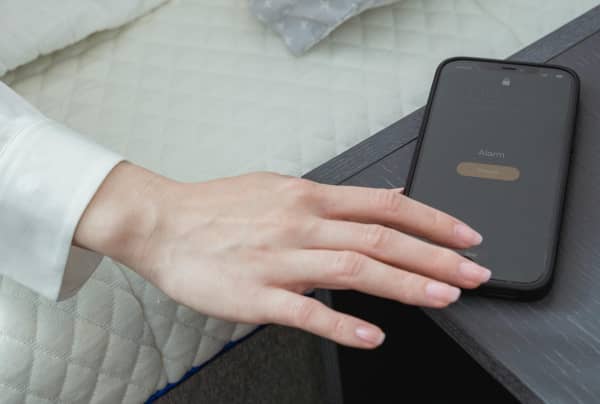 woman's hand reaches out of her bed for phone