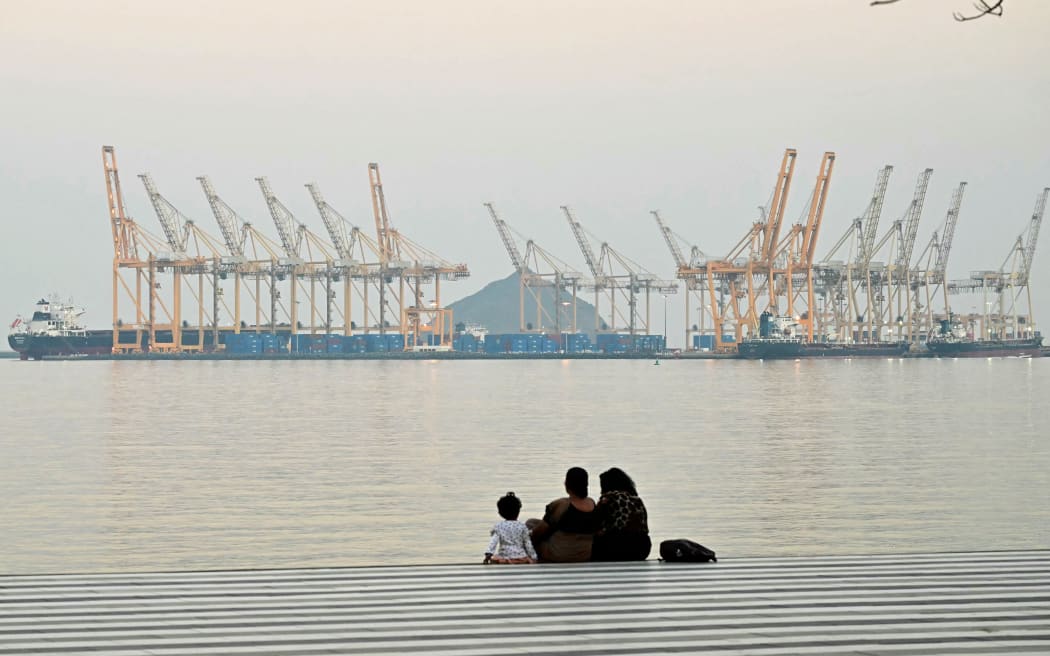 A family sits against the backdrop of a dockyard off coast city of Fujairah, in the Strait of Hormuz in the northern Emirate on February 25, 2026. (Photo by Giuseppe CACACE / AFP)