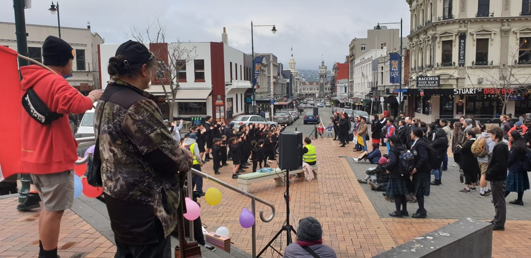 Protesters at the Octagon in Dunedin watch as school children perform waiata.