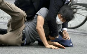 [File Photo] Tetsuya YAMAGAMI is held down by a police officer after shooting Japanese former Prime Minister Shinzo ABE in Nara, Japan, on July 8, 2022. Nara District Court sentenced YAMAGAMI this afternoon to an unlimited imprisonment. The 45-year-old defendant has been charged with murder and other crimes for allegedly killing former Prime Minister Shinzo Abe with a homemade firearm during a campaign speech for supporting a candidate in the 2022 House of Councilors election in Nara City.  The trial has been held 15 times since the first hearing on October 28, 2025. While the prosecution has sought an unlimited sentence, the defense has maintained that the sentence should be limited to 20 years. ( The Yomiuri Shimbun ) (Photo by Kazuhiko HIRANO / The Yomiuri Shimbun via AFP)
