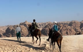 Two horses carry tourists over the desert landscape of Jordan