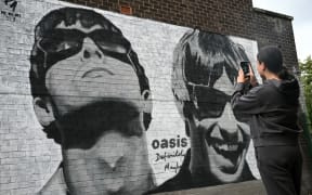 An Oasis fan takes a photo at a new mural by Pic.One.Art, of Oasis' Liam and Noel Gallagher on the side of a record store in Manchester, northern England, on 27 August, 2024, the day the band announced they will re-form and tour.