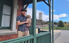 Social studies teacher Kyle Webb with his dog Huxley at the war memorial education centre, with the carillon bell tower behind them.