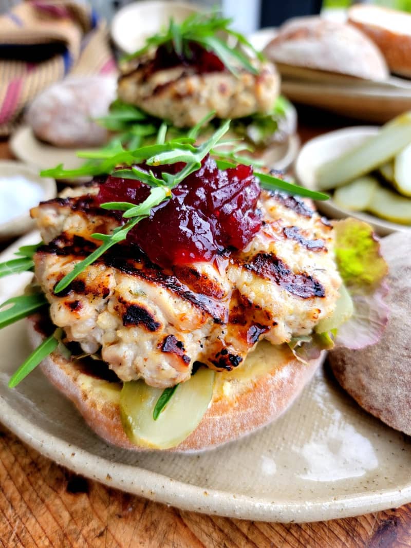 An image of turkey burgers, featuring a turkey mince pattie, topped with cranberry sauce and garnished with rocket leaves.