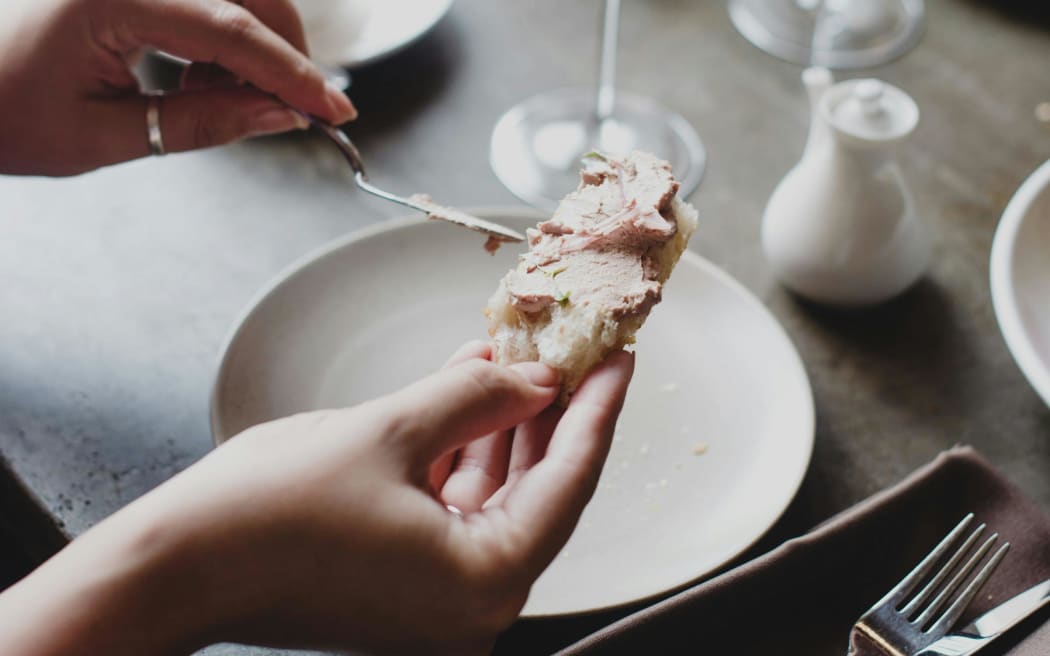 A person spreads pate on a piece of bread
