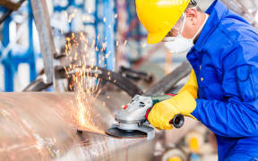 Industrial worker in manufacturing plant grinding to finish a pipeline.