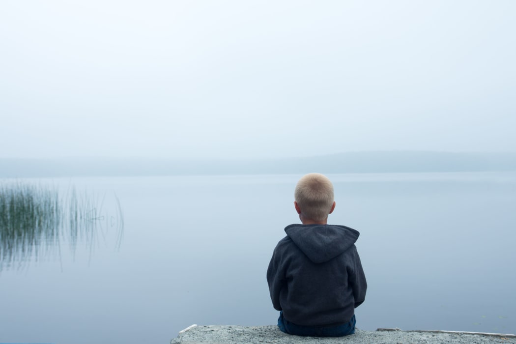 47556115 - sad child sitting alone by lake in a foggy day, back view