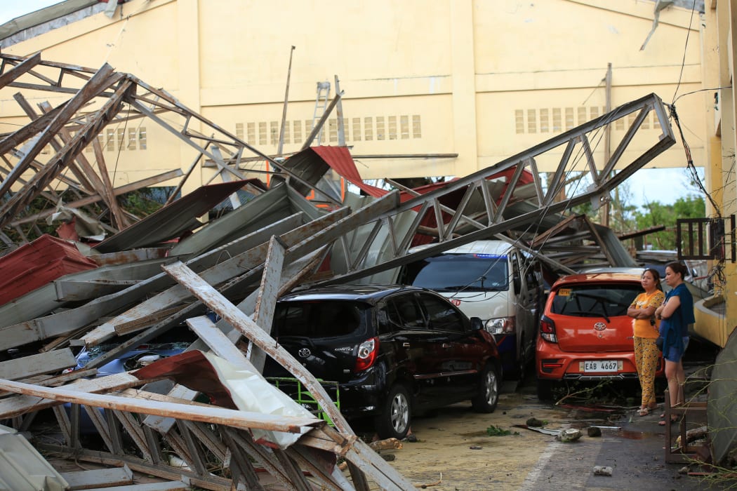 Residents stand next to cars damaged after a gymnasium collapsed at the height of super Typhoon Goni after it hit Tabaco, Albay province, south of Manila on November 1, 2020.