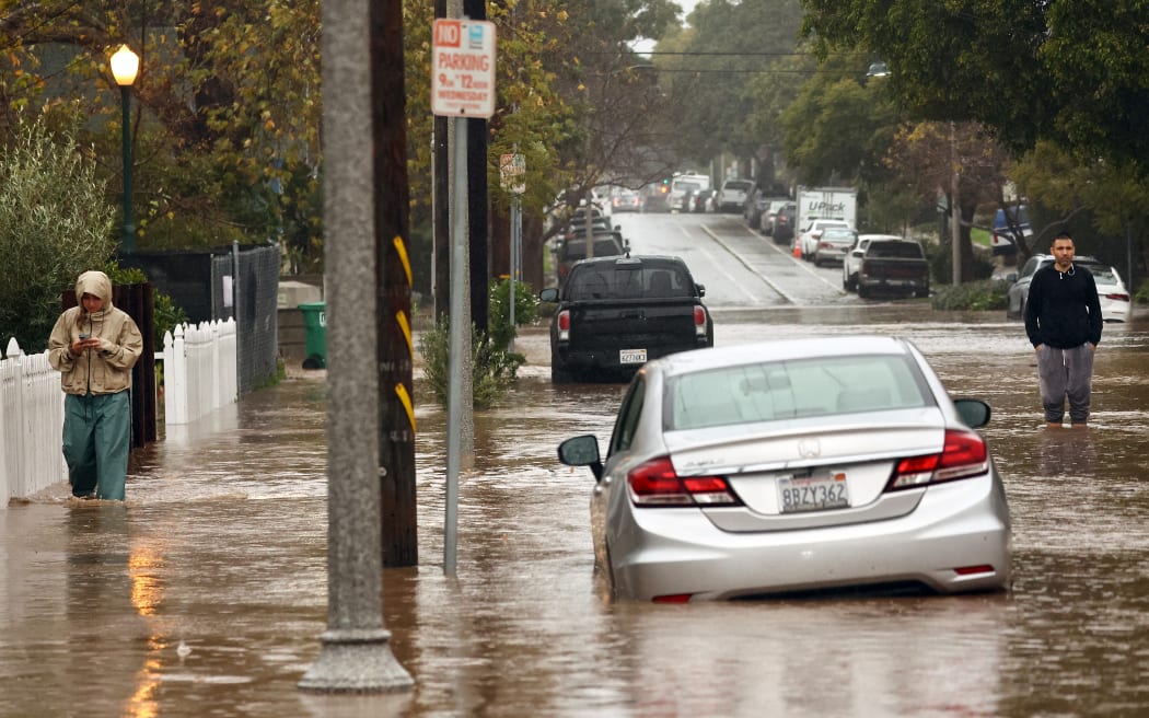 SANTA BARBARA, CALIFORNIA - FEBRUARY 04: People gather along a flooded street as a powerful long-duration atmospheric river storm, the second in less than a week, impacts California on February 4, 2024 in Santa Barbara, California. The storm is delivering potential for widespread flooding, landslides and power outages while dropping heavy rain and snow across the region.   Mario Tama/Getty Images/AFP (Photo by MARIO TAMA / GETTY IMAGES NORTH AMERICA / Getty Images via AFP)