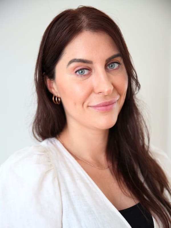 Carly Dober - a dark haired woman with blue eyes - smiles slightly at the camera.