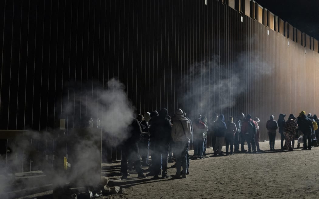 Asylum-seekers line up to be processed by US Customs and Border Patrol agents at a gap in the US-Mexico border fence near Somerton, Arizona, on 26 December, 2022.