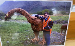 Sincere Standtrue is pictured wearing hi-vis clothing, posing with a sculpture of a moa in one of the images on display in the Greymouth courtroom where the inquest into his death is taking place.