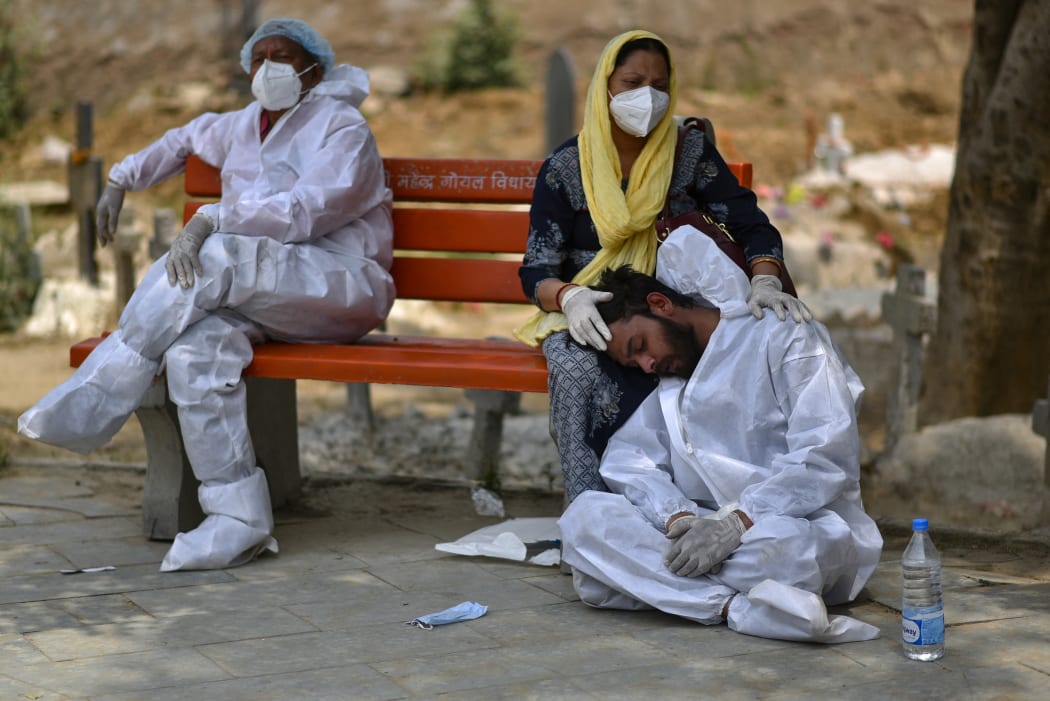An exhausted health worker wearing personal protective equipment rests at a bench at a graveyard, in Delhi, India
