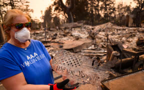 Danielle Maki displays an item she found in the remains of her brother's home burned in the Eaton fire in the Altadena area of Los Angeles county, California on January 9, 2025. Massive wildfires that engulfed whole neighborhoods forcing over 100,000 people to flee their homes and claiming at least five lives in Los Angeles remained totally uncontained on January 9, authorities said, as US National Guard soldiers readied to hit the streets to help quell disorder. (Photo by JOSH EDELSON / AFP)