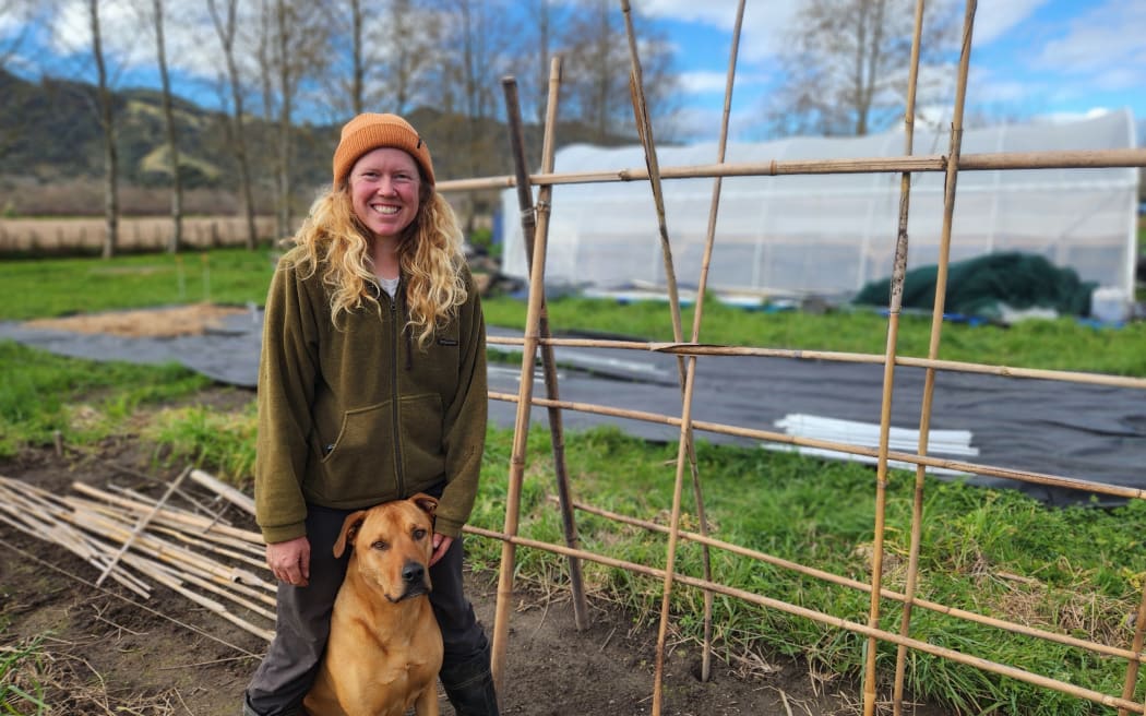 Jemma standing in front of her greenhouse with her dog at her feet