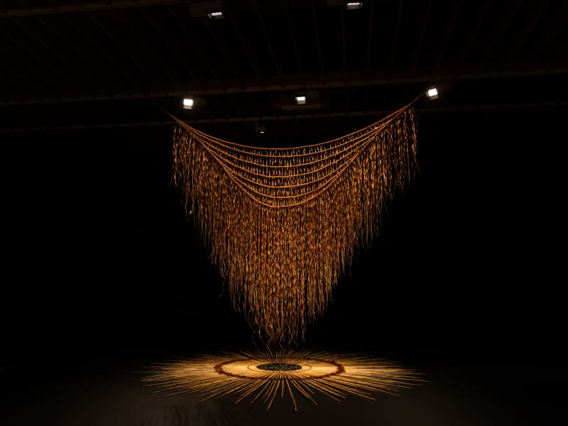 A giant piece of delicate brown weaving is illuminated by lights.