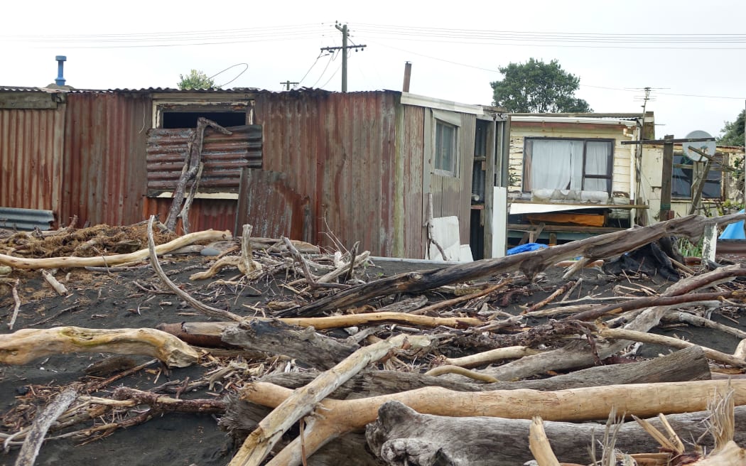 Big pieces of drift wood pile up near to corrugated shed and old beach home.