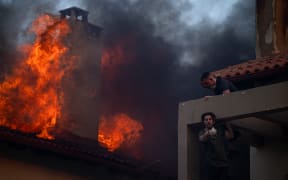 Local residents try to extinguish the fire of a burning house during a wildfire in Kryoneri, near Athens on July 26, 2025. Greece has already been hit by a series of heatwave-fuelled wildfires this summer, including one that forced the closure of the Acropolis in Athens, its top archaeological monument, earlier this month. (Photo by Angelos TZORTZINIS / AFP)