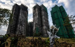 Flowers are seen in front of the Wang Fuk Court apartment blocks in the aftermath of the deadly November 26 fire in Hong Kong's Tai Po district on December 3, 2025. The death toll in Hong Kong's deadliest fire in decades has risen to 159 after all affected housing blocks have been searched, police said December 3, cautioning that the figure may not be final. (Photo by Philip FONG / AFP)