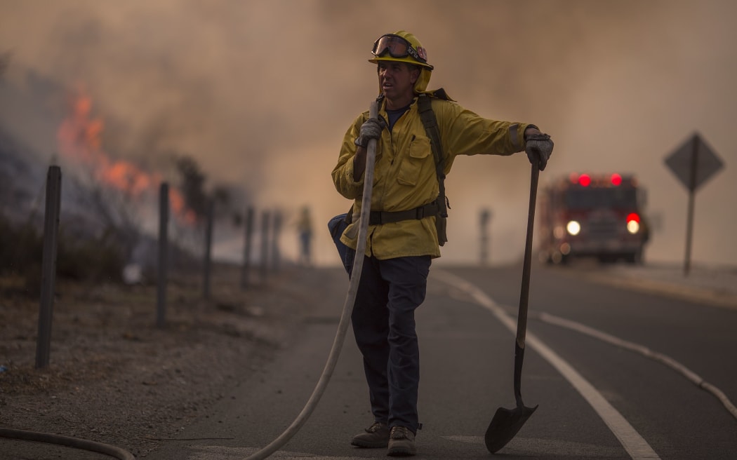A firefighter holds a hose on the 120 freeway during fight against the La Tuna Fire.