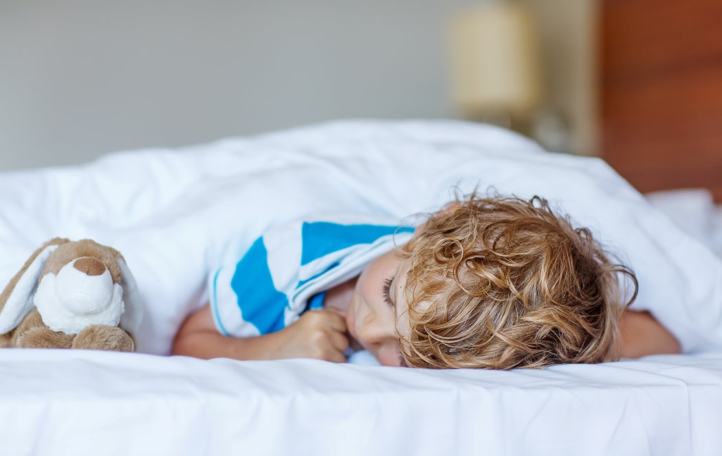 Adorable child sleeping and dreaming in his white bed with toy.