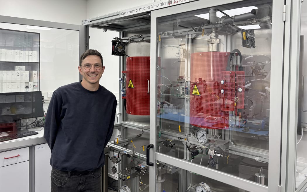 Dr Lucjan Sajkowski stands next to a glass cabinet housing Earth Sciences New Zealand's new geothermal process simulator.