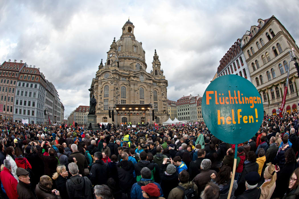 A sign reading "Help the refugees!" in the foreground as thousands of people take part in a rally themed: "For Dresden, for Saxony - living together in the sense of a global awareness, humanity and dialogue".