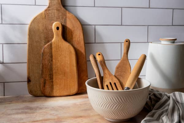 Wooden spatulas, rolling pin and spoon in a bowl, and wooden chopping boards propped up.