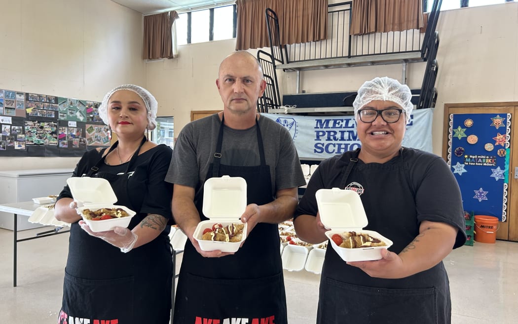 The photo depicts three people holding lunch boxes, showing what children at Melville Primary School will have for lunch.