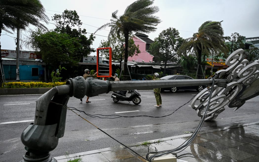 Residents make their way past a lamp post that collapsed in strong winds ahead of the arrival of Typhoon Kalmaegi near Quy Nhon beach in Gia Lai province in central Vietnam on November 6, 2025. Typhoon Kalmaegi's windspeeds were increasing November 6 as it headed towards neighbouring Vietnam, where fear was mounting the typhoon could compound the damage of a week of flooding that has already claimed 47 lives. (Photo by NHAC NGUYEN / AFP)