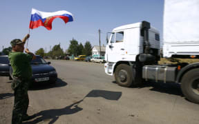 A resident holds a Russian national flag as lorries, part of a Russian humanitarian convoy cross the Ukrainian border.