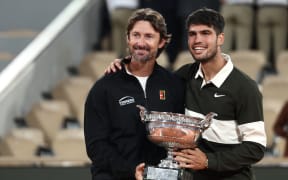 (FILES) Spain's Carlos Alcaraz poses with his Spanish coach Juan Carlos Ferrero (L) after winning against Italy's Jannik Sinner at the end of their men's singles final match on day 15 of the French Open tennis tournament on Court Philippe-Chatrier at the Roland-Garros Complex in Paris on June 8, 2025. Men's tennis world number one Carlos Alcaraz announced on December 17, 2025 on social media he is splitting from his coach Juan Carlos Ferrero after seven hugely successful years. (Photo by Thibaud MORITZ / AFP)