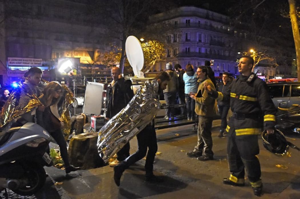 People wearing survival blankets walk by a rescuer near the Bataclan concert hall in central Paris,