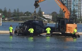 In this handout photo taken and released on January 3, 2023 airport workers prepare to remove a crashed helicopter that collided with another helicopter in Gold Coast on January 2, killing four. A British couple were among four killed in a mid-air collision that left two mangled helicopters on a sandbank near an Australian tourist hotspot, investigators said. (Photo by Handout / ABC / AFP) / - Australia OUT / - AUSTRALIA OUT / RESTRICTED TO EDITORIAL USE - MANDATORY CREDIT “ AFP PHOTO / ABC” - NO MARKETING - NO ADVERTISING CAMPAIGNS - DISTRIBUTED AS A SERVICE TO CLIENTS