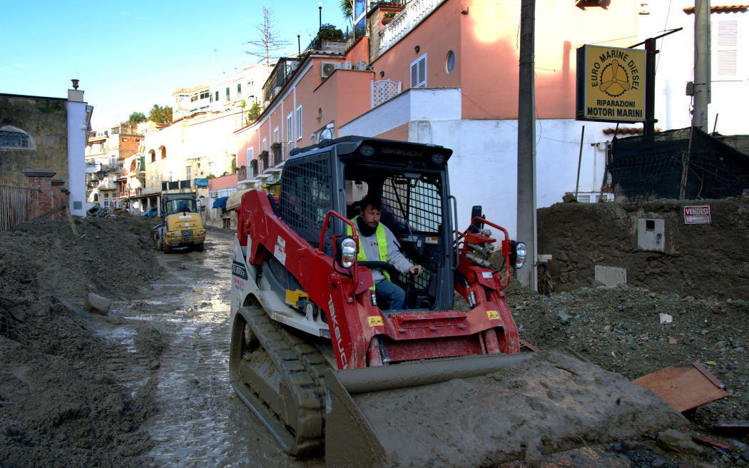 A man uses a tractor to remove mud from a street in Casamicciola on November 27, 2022, following heavy rains that caused a landslide on the island of Ischia, southern Italy. - Italian rescuers were searching for a dozen missing people on the southern island of Ischia after a landslide killed at least one person, as the government scheduled an emergency meeting. A wave of mud and debris swept through the small town of Casamicciola Terme early Saturday morning, engulfing at least one house and sweeping cars down to the sea, local media and emergency services said.