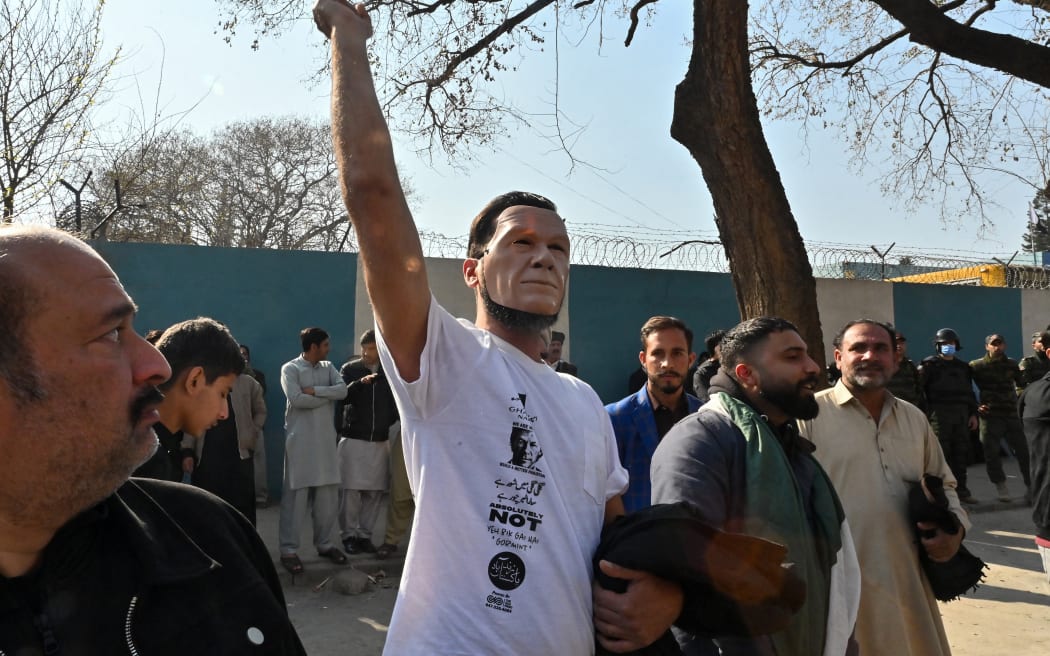 A supporter of the Pakistan Tehreek-e-Insaf (PTI)party, wearing a face replica of jailed former prime minister and party leader Imran Khan, shout slogans in a protest in Islamabad on February 11, 2024, amid claims the election result delay is allowing authorities to rig the vote-counting. Pakistan police warned Sunday they would come down hard on illegal gatherings after the party of jailed former prime minister Imran Khan urged supporters to protest alleged rigging in last week's election. (Photo by Farooq NAEEM / AFP)