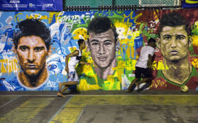 Locals play football in front of a mural of soccer stars Lionel Messi (left), Neymar da Silva Santos Junior (centre) and Christiano Ronaldo at a field in a Rio de Janeiro favela.