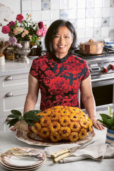 Jane Barnes is a smiling woman wearing a tight red t-shirt standig in front of a large glazed ham.