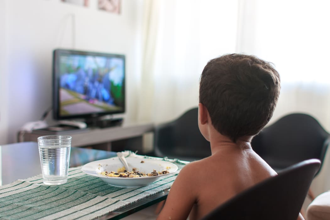 A young boy distracted watching TV while eating lunch