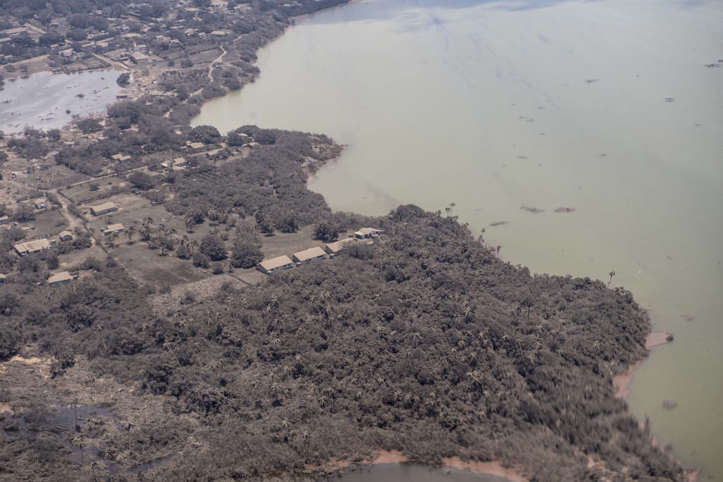 A P-3K2 Orion aircraft flies over an area of Tonga that shows Ash on homes and surrounding vegetation.