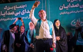 Masoud Pezeshkian, one of the two candidates qualifying for the second round of the Iranian presidential election, raises his hand on the stage in a gathering of his supporters in Tehran, Iran, on July 3, 2024. Iran is holding snap presidential elections to choose the next president after the death of Ebrahim Raisi in a helicopter crash. After the election with a historically low turnout on Friday, Masoud Pezeshkian, Iran's presidential election candidate and former reformist member of the Iranian parliament, and Saeed Jalili, Ultraconservative former nuclear negotiator will face off in a runoff presidential election on July 5. (Photo by Khoshiran / Middle East Images / Middle East Images via AFP)