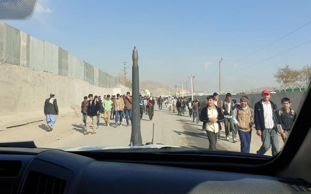 A busy street in Kabul. The photo is taken from within a car. People walk in both directions down the street.