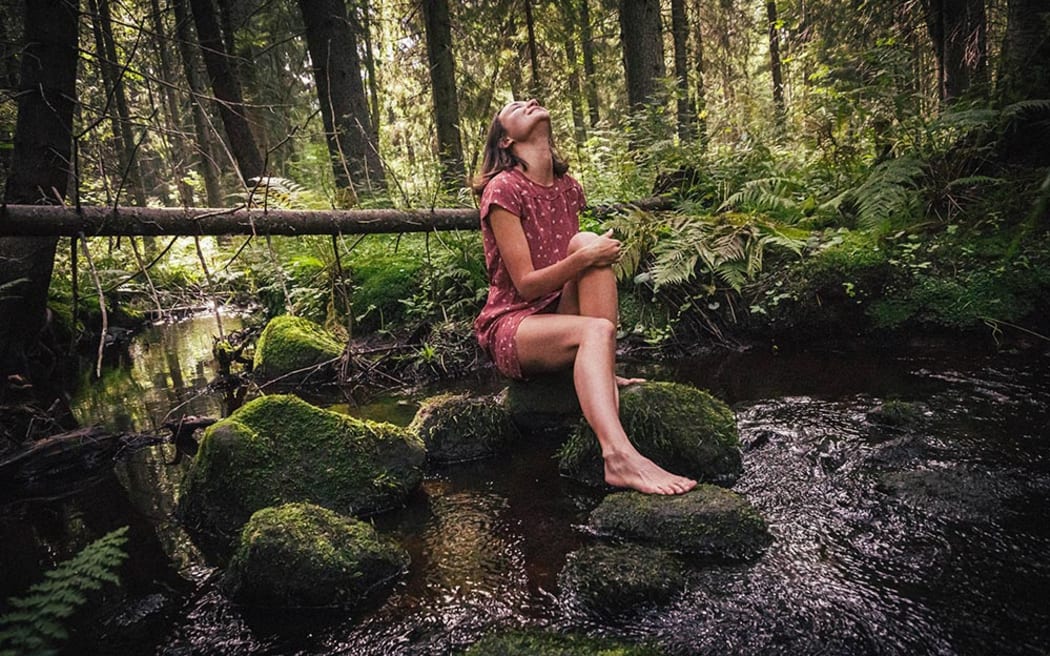 A white female with bare legs sits on moss while looking upwards