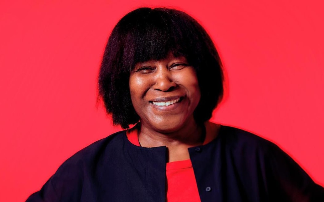 Joan Armatrading smiling with a red background
