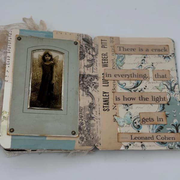 A journal open on a page with a framed photo of a young girl and a quote that reads "There is a crack in everything, that is how the light gets in."