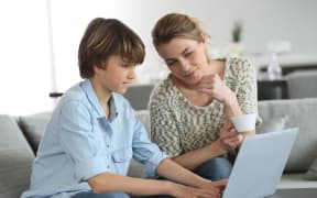 Mother looking after son doing homework on laptop