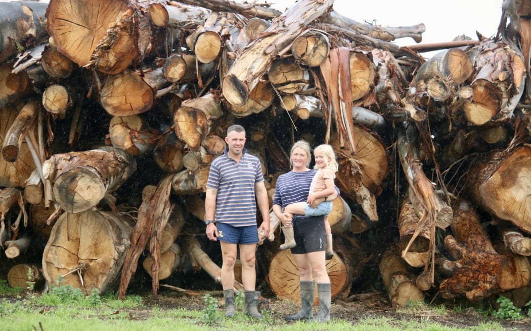 Todd and Holly McCammon with their daughter Isla, and some of the hundreds of trees that fell on their farm in October.